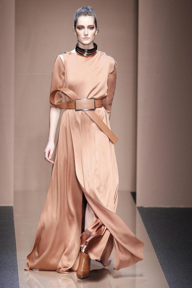 Eine Frau präsentiert ein lachsfarbenes Kleid mit Gürtel und Halsband auf dem Laufsteg.