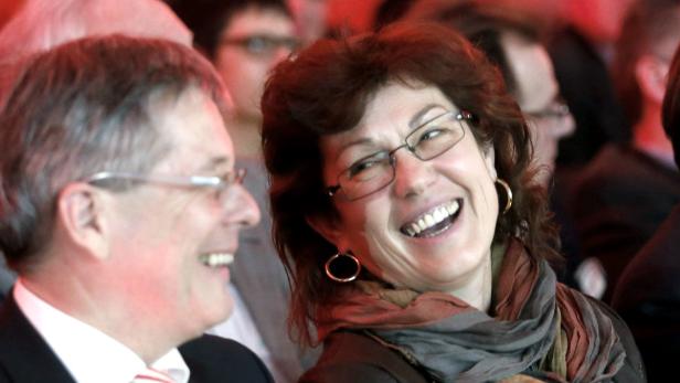 Eine lachende Frau mit Brille und Schal neben einem Mann mit Anzug.