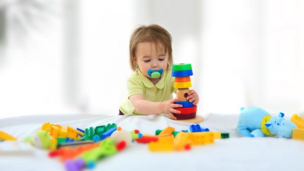 Ein Kleinkind mit Schnuller spielt mit einem bunten Stapelturm.