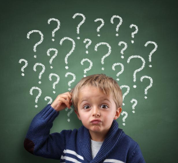 Ein nachdenklicher Junge steht vor einer Tafel mit Fragezeichen.