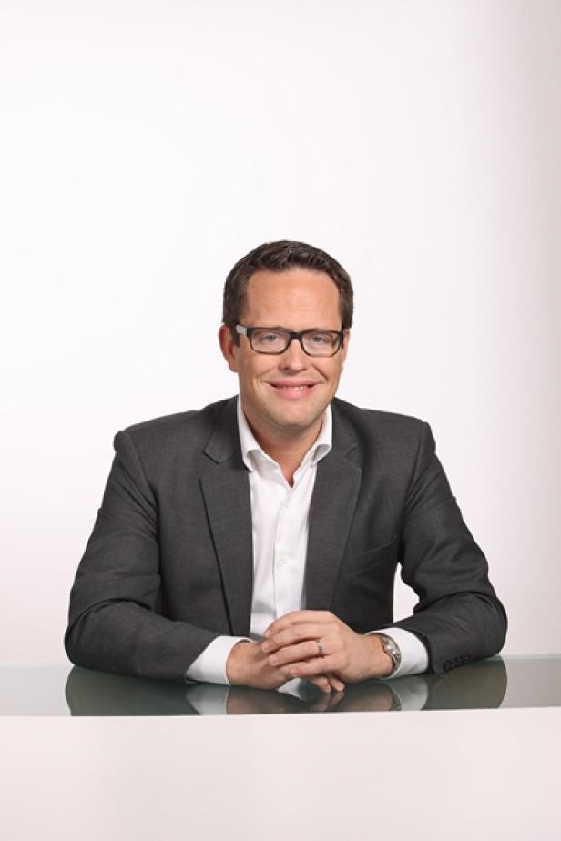 Ein Mann mit Brille und Anzug sitzt an einem Tisch.