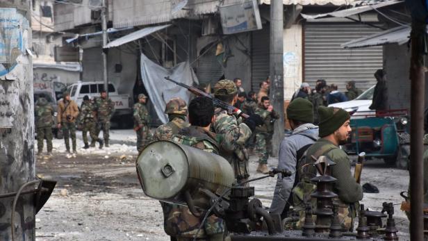 Bewaffnete Männer in Militärkleidung stehen in einer städtischen Umgebung.