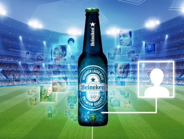 Eine Heineken-Flasche vor dem Hintergrund eines Fußballstadions mit Zuschauerporträts.
