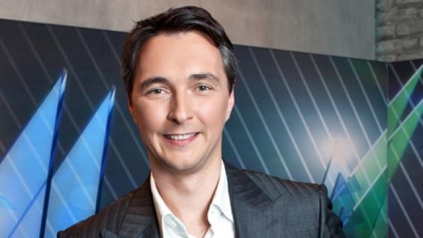 Ein lächelnder Mann in einem Anzug vor einem grafischen Hintergrund.
