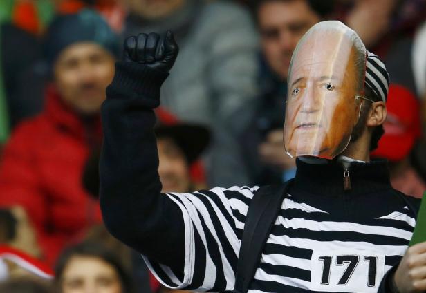 Ein Mann mit einer Maske und erhobener Faust steht in einer Menschenmenge.