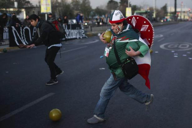Zwei Männer rennen auf einer Straße mit gelben Bällen, einer trägt mexikanische Kleidung.