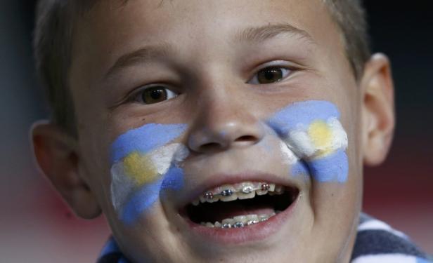 Ein Junge mit argentinischer Flagge auf den Wangen und Zahnspange lacht.