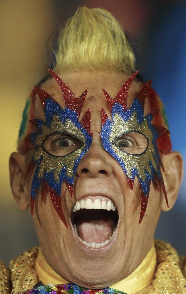 Ein Mann mit geschminktem Gesicht und offenem Mund blickt in die Kamera.