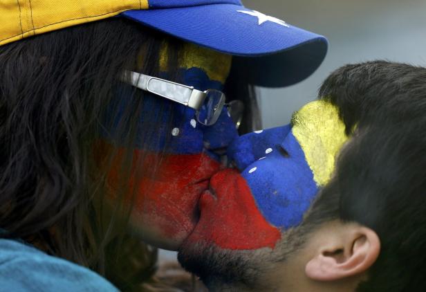 Ein Paar mit den Farben Venezuelas im Gesicht küsst sich.