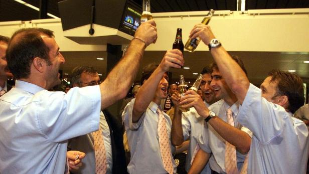 Eine Gruppe Männer in Hemden und Krawatten stößt mit Bierflaschen an.