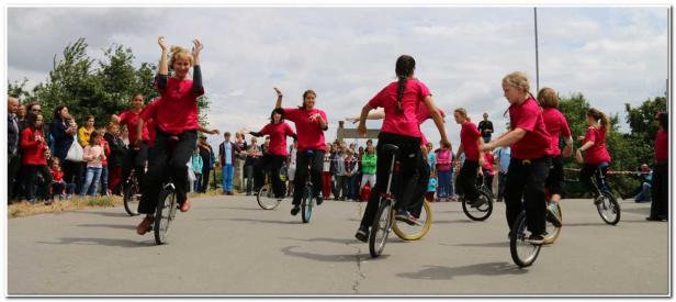 Eine Gruppe von Mädchen in roten T-Shirts fährt Einrad vor einer Zuschauermenge.