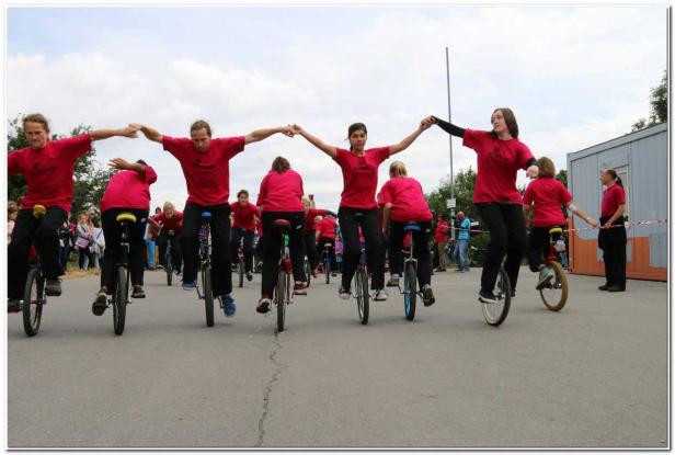 Eine Gruppe von Personen in roten T-Shirts fährt Einrad und hält Händchen.