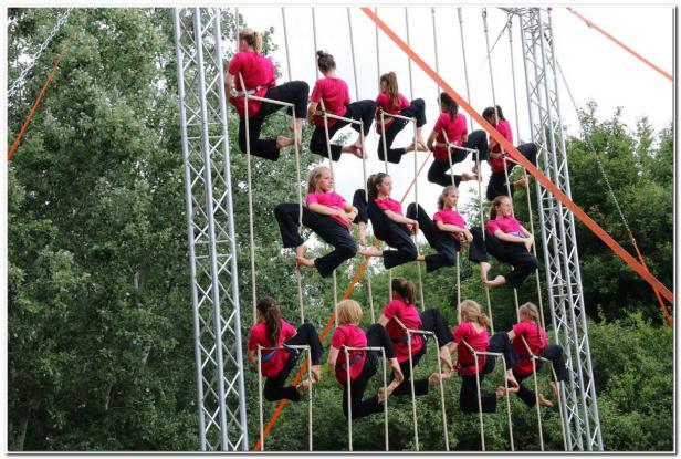 Eine Gruppe Mädchen in pinkfarbenen T-Shirts sitzt auf einer Kletterkonstruktion im Freien.