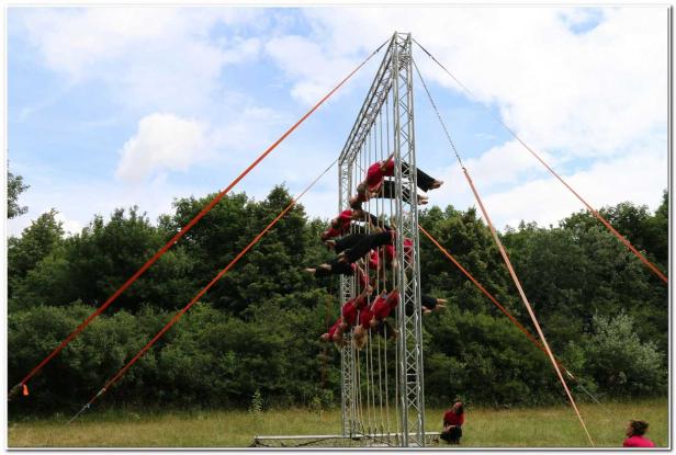 Eine Gruppe von Artistinnen hängt an einem Metallgerüst vor einer grünen Baumkulisse.