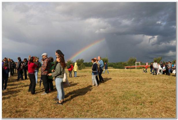 Eine Gruppe von Menschen steht auf einem Feld unter einem Regenbogen.