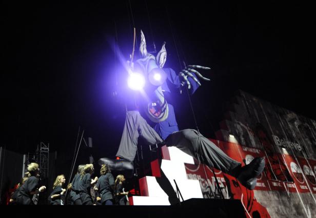 Eine riesige, puppenspielartige Figur mit leuchtenden Augen auf einer Bühne.