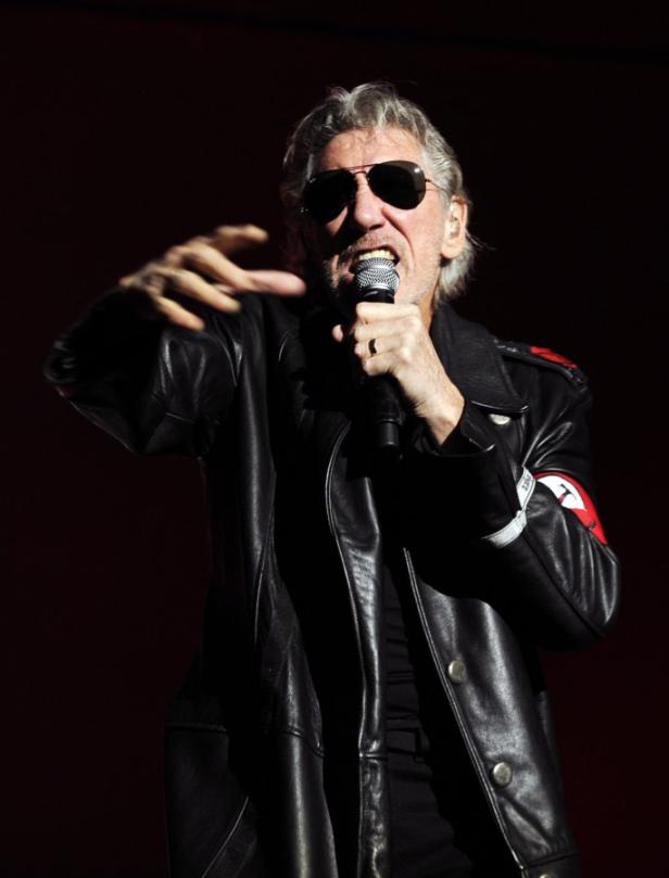 Roger Waters tritt in einer schwarzen Lederjacke mit Armbinde auf und singt in ein Mikrofon.