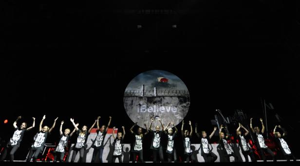 Eine Gruppe von Kindern steht auf einer Bühne vor einer Projektion mit dem Schriftzug „I Believe“.