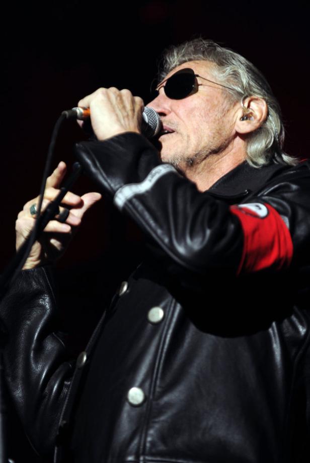 Roger Waters singt mit Sonnenbrille und roter Armbinde in ein Mikrofon.