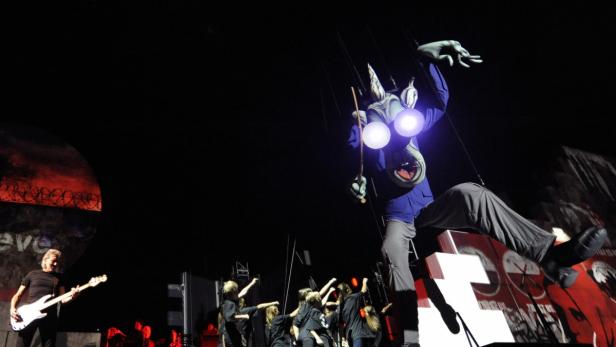 Roger Waters spielt Bassgitarre neben einer riesigen Marionette während einer Bühnenaufführung.