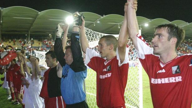 Eine Gruppe Fußballspieler feiert mit erhobenen Armen vor einem Fußballtor.