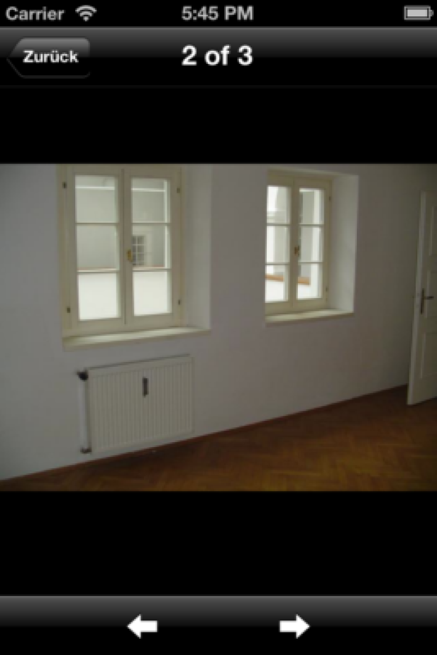 IS Immobilien - iPhone-App - Lucy Marx Ein Zimmer mit zwei Fenstern, einem Heizkörper und einem Holzboden.