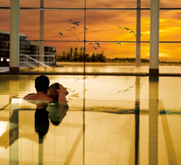 Ein Paar entspannt in einem Pool mit Blick auf einen Sonnenuntergang.