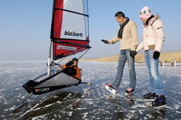 Ein Mann fährt mit einem Eissegler auf dem Eis, während ein Paar Schlittschuh läuft.