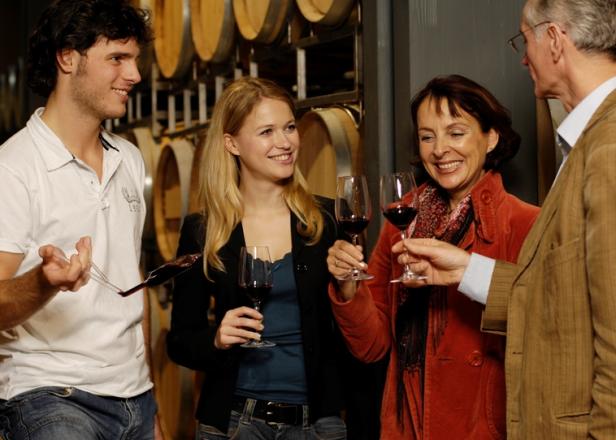 Eine Gruppe von Leuten verkostet Wein in einem Weinkeller mit Holzfässern.