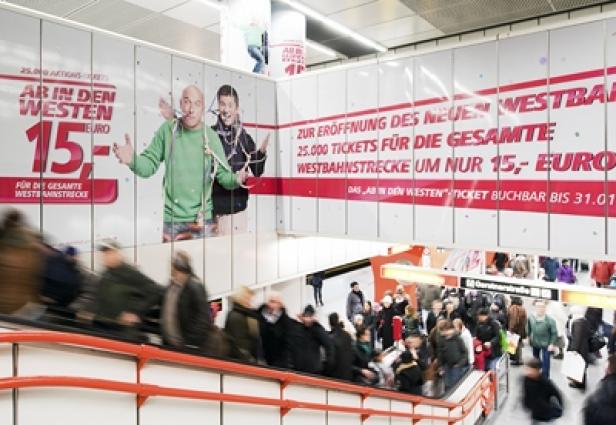 Menschen nutzen eine Rolltreppe in einer U-Bahn-Station mit Werbung für die Westbahn.