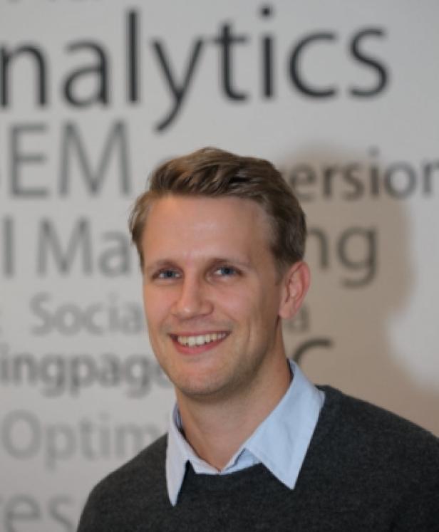 Michael Ebner, Webanalyse-Spezialist e-dialog (c: e-dialog) Ein lächelnder Mann vor einer Wand mit Begriffen aus dem Bereich Online-Marketing.