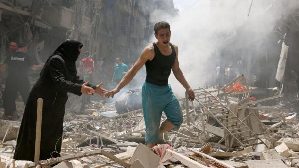 Eine Frau hilft einem weinenden Mann durch die Trümmer eines zerstörten Gebäudes.