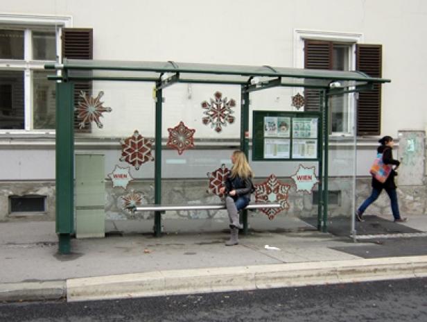 Eine Frau sitzt an einer Bushaltestelle in Wien, die mit großen Schneeflocken dekoriert ist.
