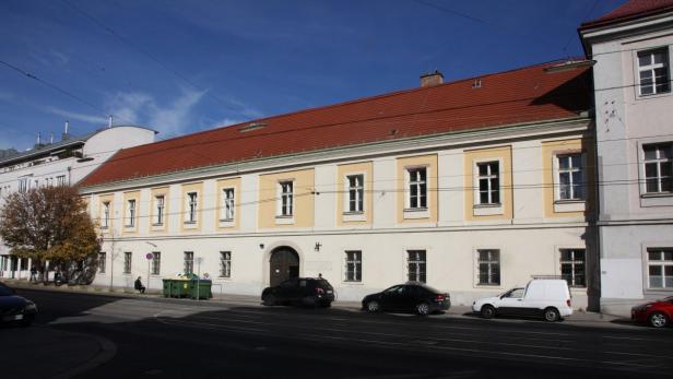 Ein langgestrecktes, gelb gestrichenes Gebäude mit rotem Ziegeldach in einer Stadt.