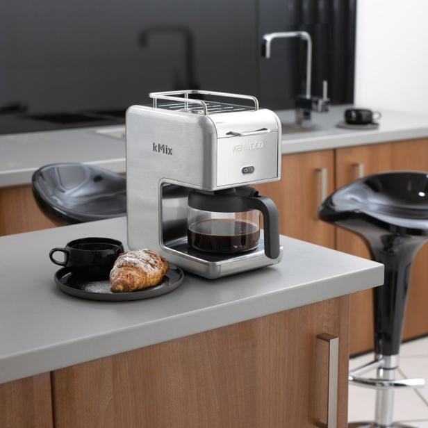Eine Kenwood kMix Kaffeemaschine mit Kaffee, einer Tasse und einem Croissant in einer Küche.