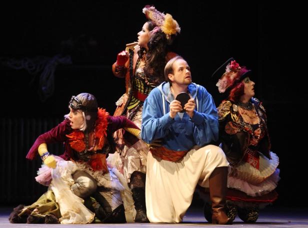 Eine Gruppe von Darstellern in extravaganten Kostümen auf einer Bühne.