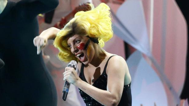 Lady Gaga singt mit gelbem Haar und Gesichtsbemalung auf der Bühne.