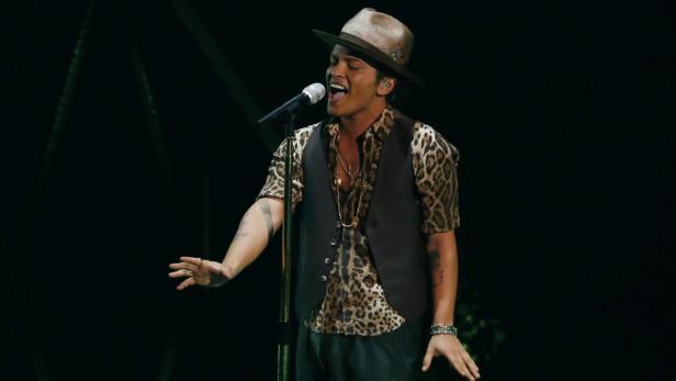 Bruno Mars tritt in einem Leopardenmusterhemd und Hut auf einer Bühne auf.