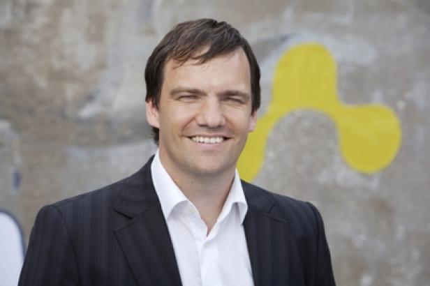 Ein lächelnder Mann im Anzug vor einer Wand mit Graffiti.