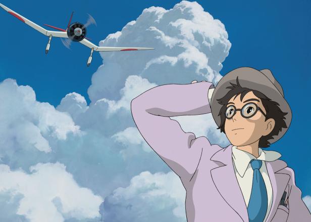 Ein junger Mann mit Hut und Brille blickt zu einem Flugzeug am Himmel.