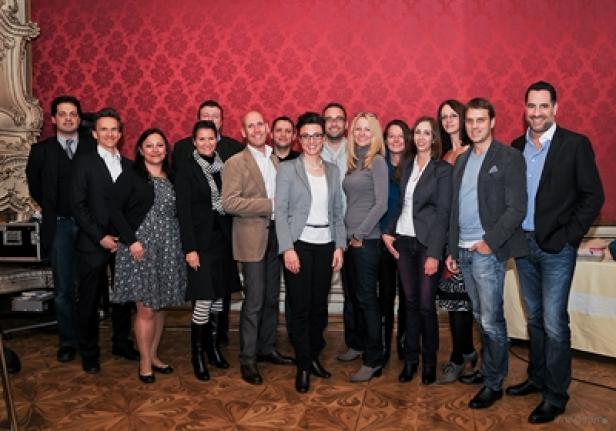 Eine Gruppe von etwa 15 Personen posiert vor einer roten Wand für ein Gruppenfoto.