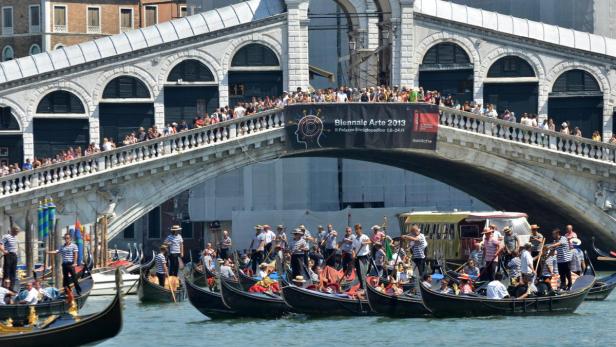 Gondeln fahren unter der Rialtobrücke in Venedig, auf der sich viele Menschen befinden.