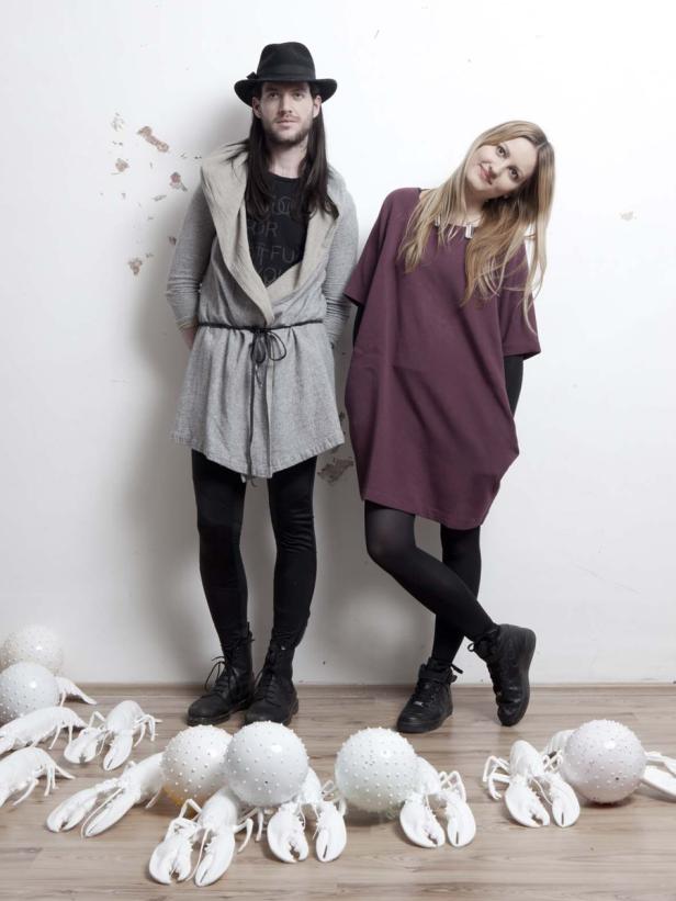 Ein Mann mit Hut und eine Frau stehen vor einer Wand, umgeben von weißen Hummer-Dekorationen.