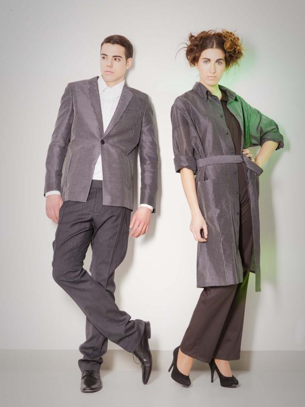 Ein Mann im Anzug und eine Frau im Mantel posieren vor einer weißen Wand.