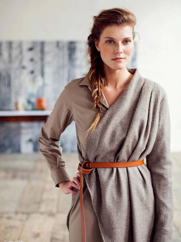 Eine Frau mit Zopf trägt ein beiges Kleid mit einem braunen Gürtel.