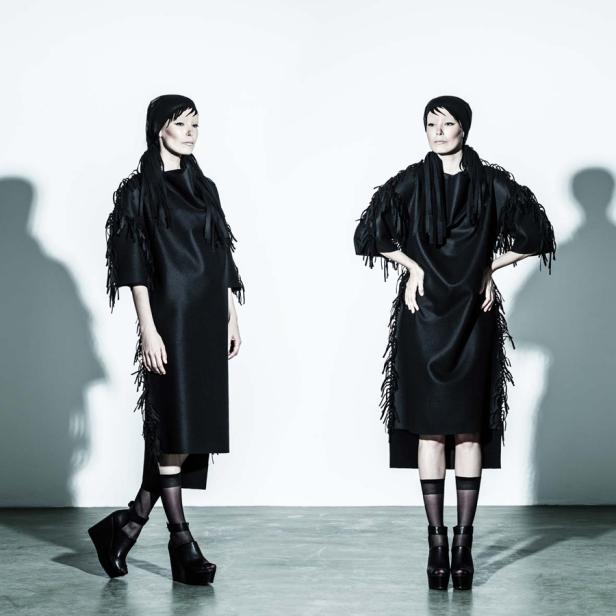 Zwei Models präsentieren ein schwarzes Kleid mit Fransen und Plateauschuhen.