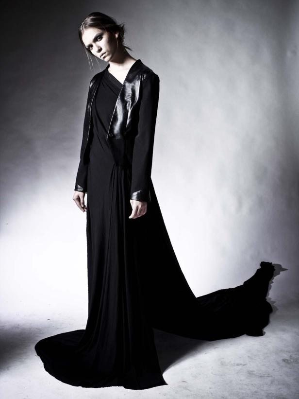 Eine Frau in einem langen, schwarzen Kleid mit Schleppe und einer Jacke mit Lederdetails.