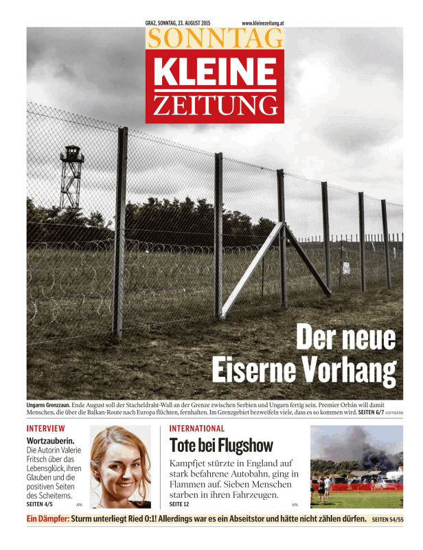Ein Grenzzaun mit Stacheldraht und einem Wachturm im Hintergrund.