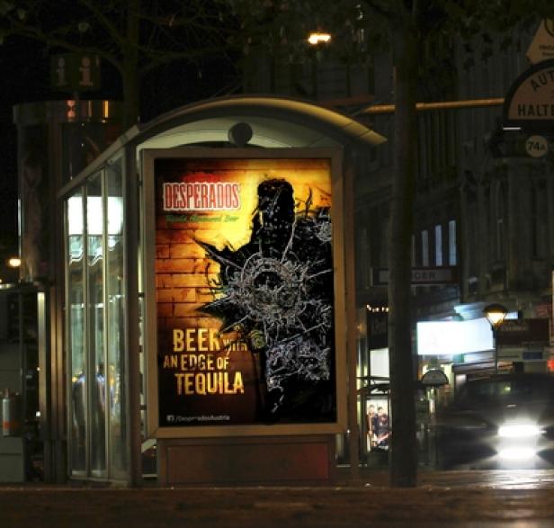 Desperados Bier - Heineken - Super-Fi Eine Bushaltestelle mit einer Werbung für Desperados Tequila-Bier bei Nacht.
