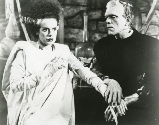 Eine Schwarzweißaufnahme von der Braut und Frankenstein, die Hände halten.